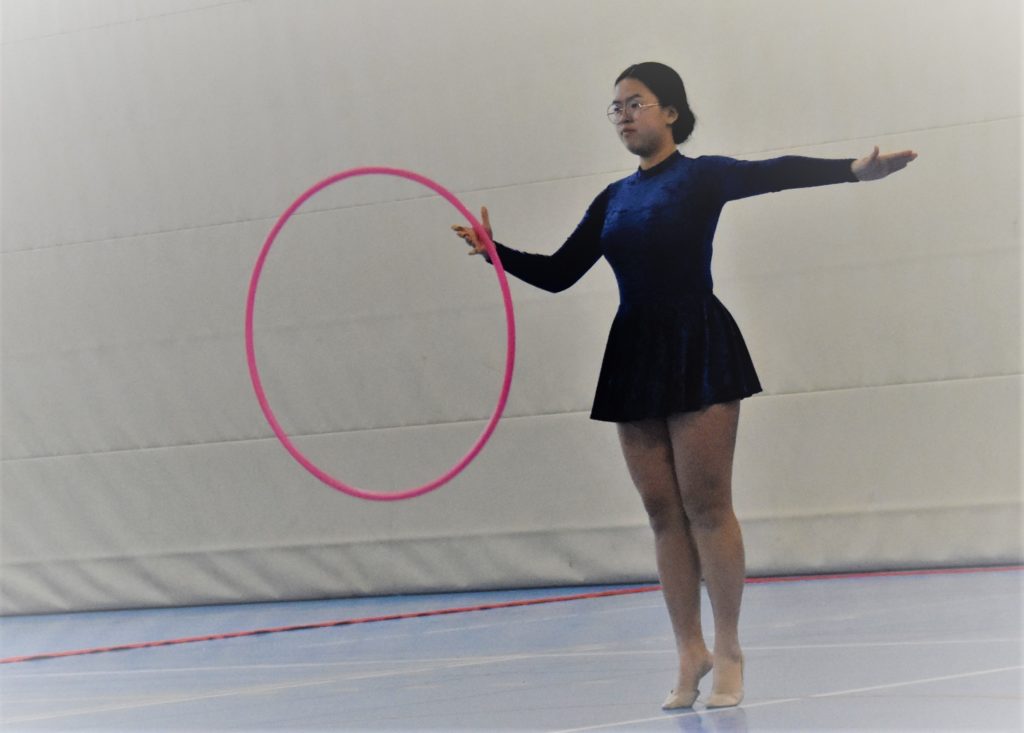 gymnaste sur la pointe des pieds tenant un cerceau rose devant elle dans la main droite